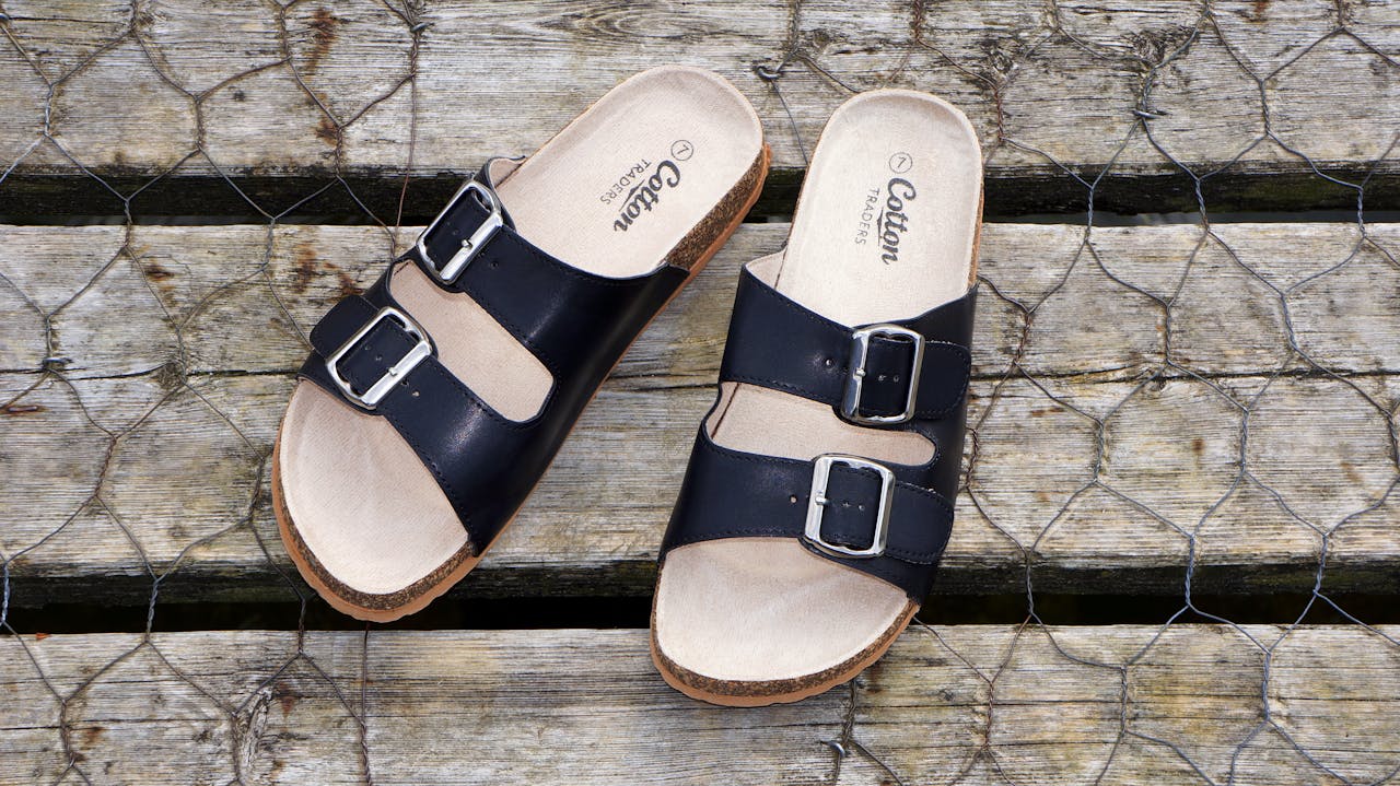 about-01 Black leather buckle sandals on a wooden surface, perfect for casual summer fashion.
