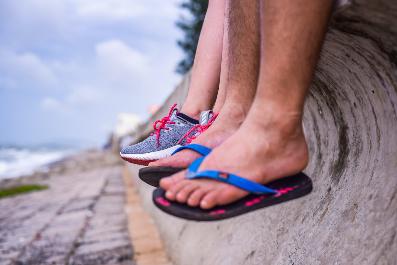 hero-img-02 Feet in sneakers and flip-flops resting on a seaside wall with ocean view.